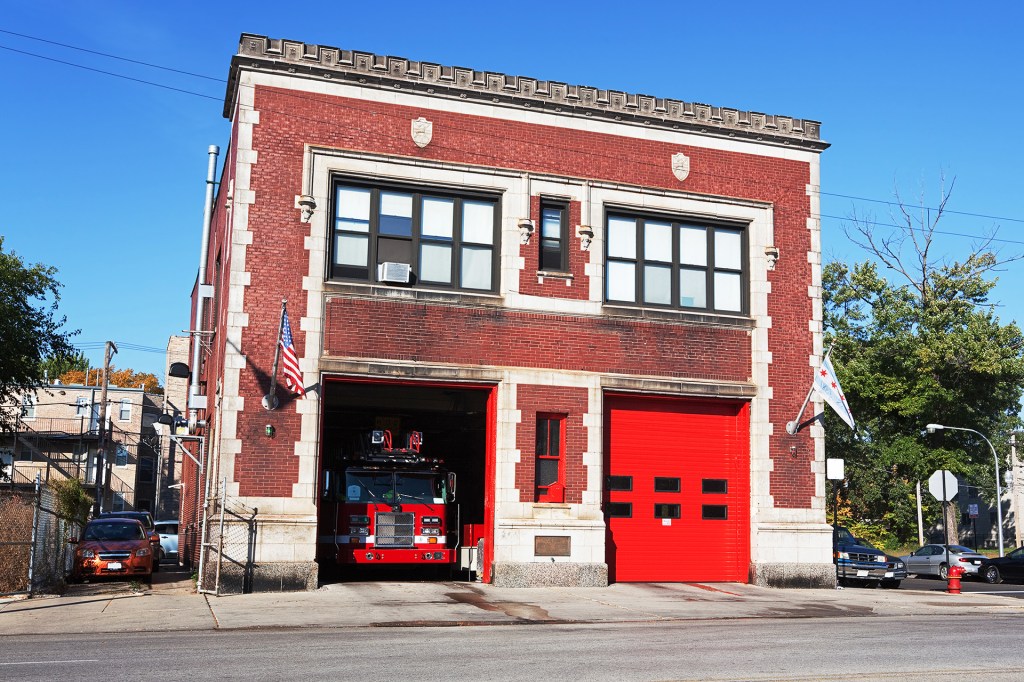 A fire truck sits inside a brick fire station with bright red garage doors.