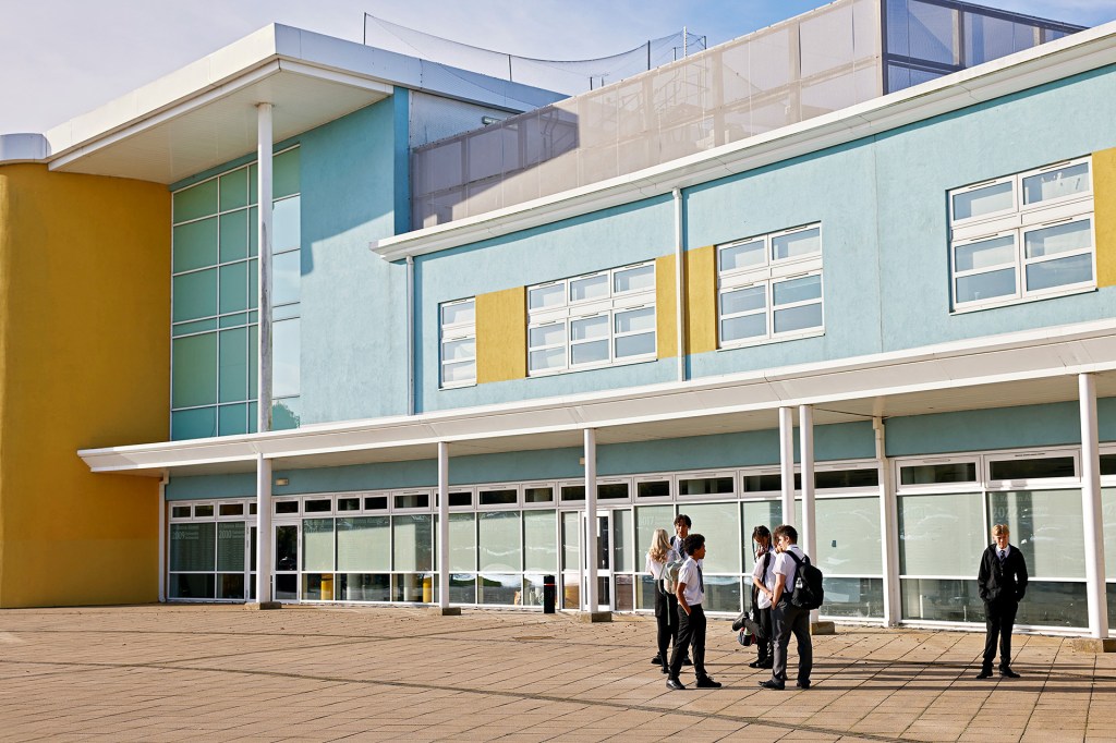 Students stand outside a school building on a sunny day.