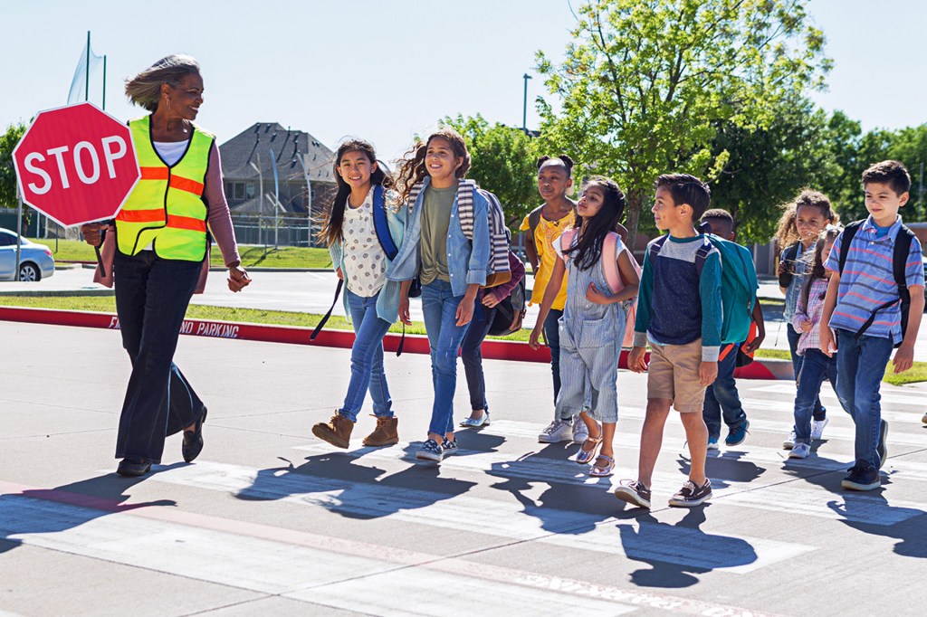 A crossing guard leads a group of children safely across the street.