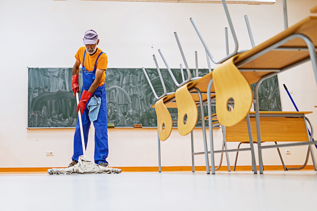 A custodian mops the floor in an empty classroom.