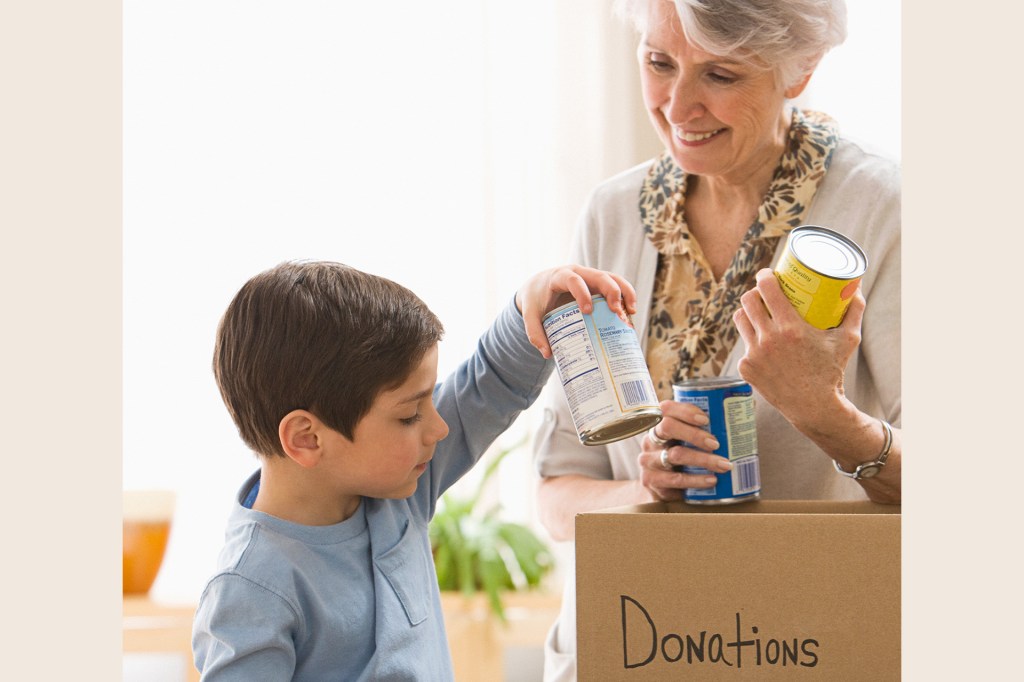 A child places canned food into a donation box while an older adult holds more cans.