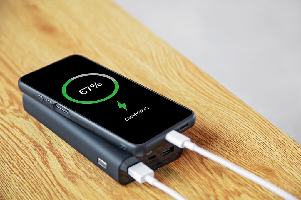 A smartphone charges while resting on a portable battery pack.