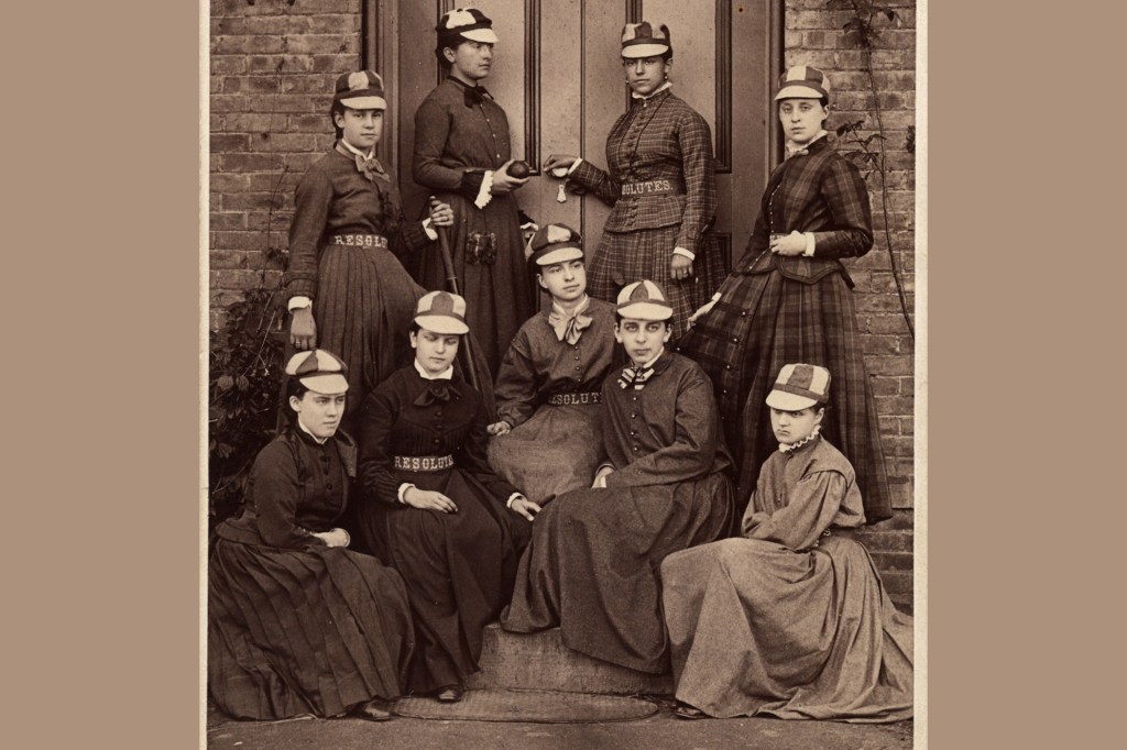 In an old photo, nine women wearing matching baseball caps pose together.