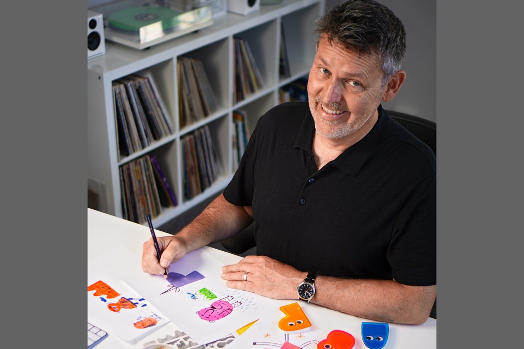 An author smiles while drawing colorful characters at a table.