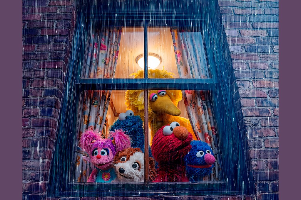 A group of puppet characters look out a window together as rain falls outside.