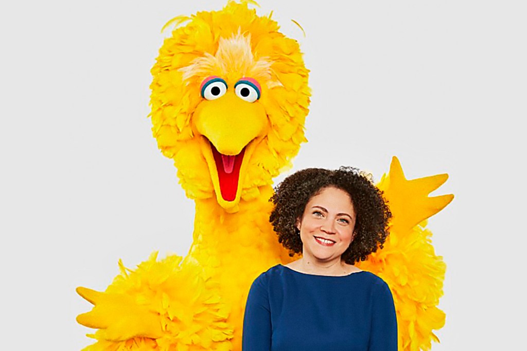 A smiling woman poses in front of a big yellow bird puppet.