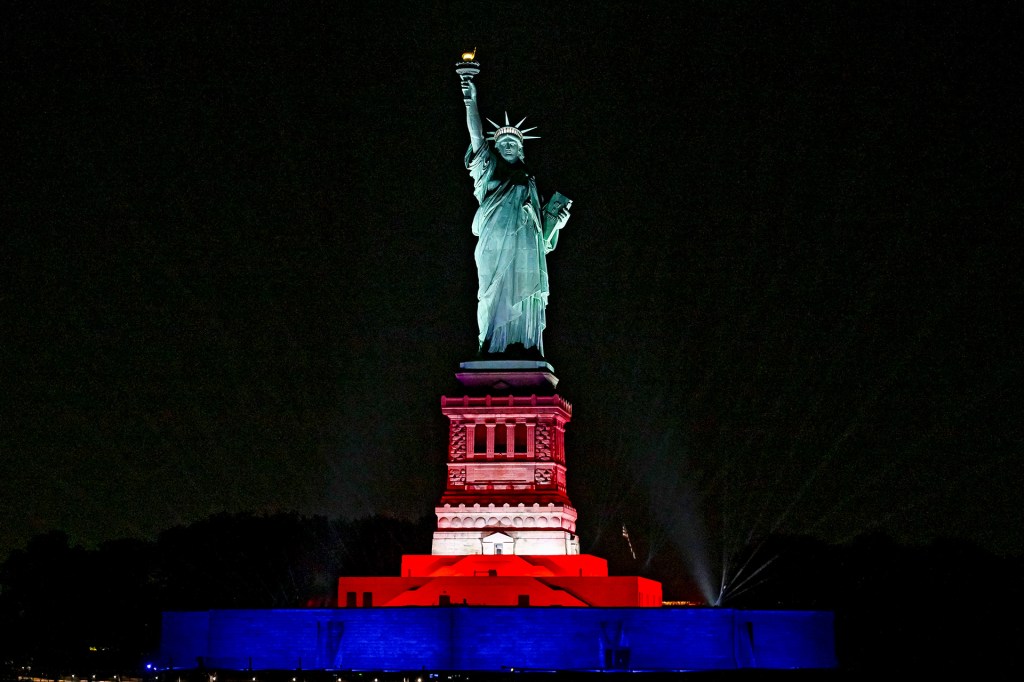 The Statue of Liberty is lit in red, white, and blue against the night sky.