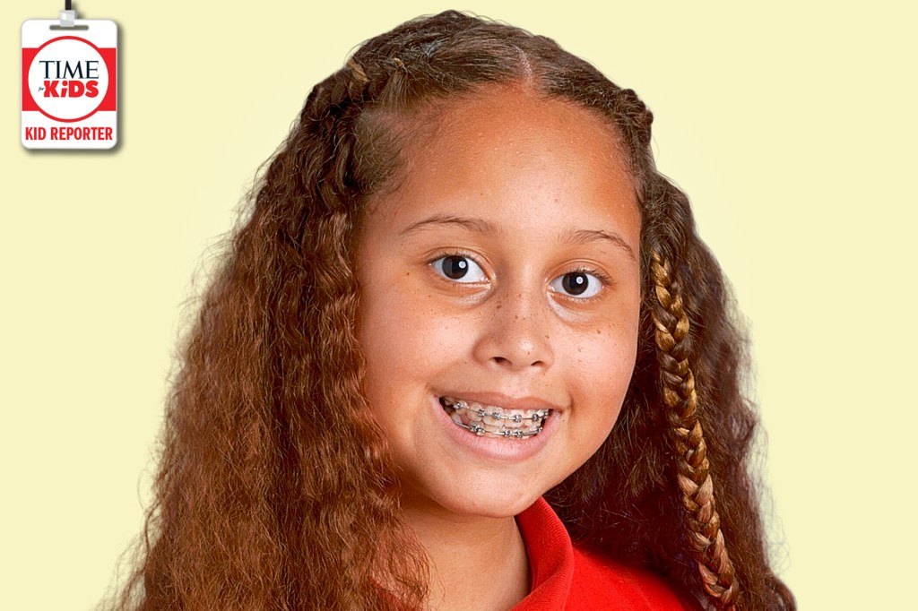 A smiling girl with long curly hair, braids, and braces poses against a pale yellow background with a TIME for Kids Kid Reporter badge.