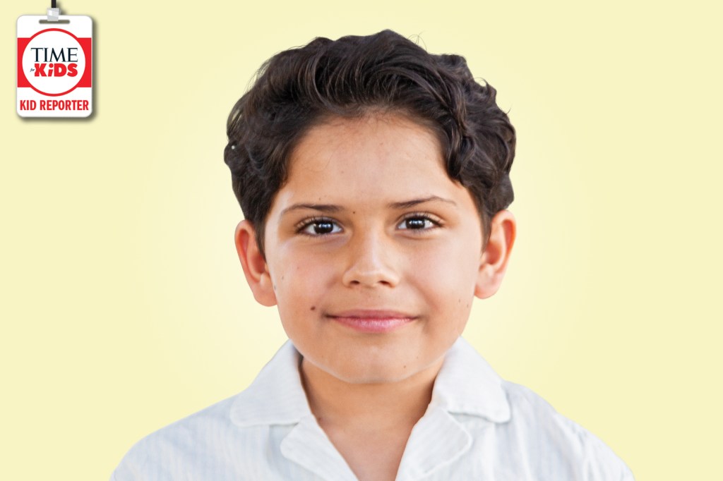 A smiling boy with short wavy dark hair poses against a pale yellow background with a TIME for Kids Kid Reporter badge.