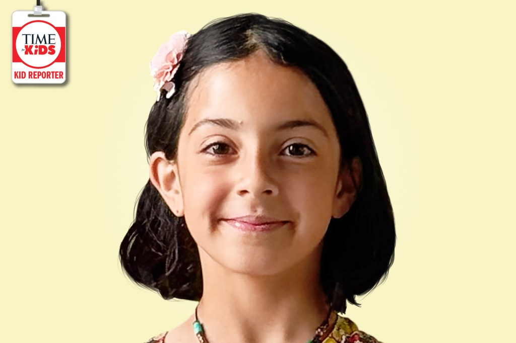A smiling girl with short dark hair and a pink flower clip poses against a pale yellow background with a TIME for Kids Kid Reporter badge.