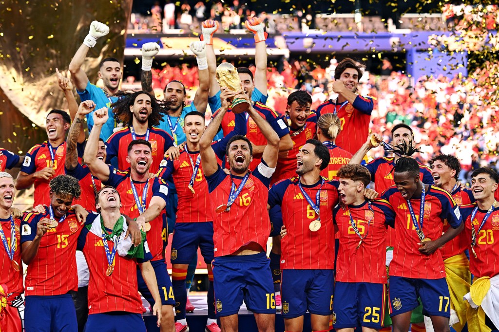 Soccer players in red uniforms celebrate as one player holds a gold trophy above his head.
