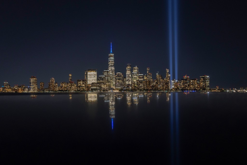 A city skyline glows at night as two beams of blue light shine straight into the sky.
