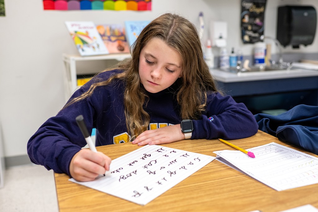 A girl sits at a desk, practicing handwriting.