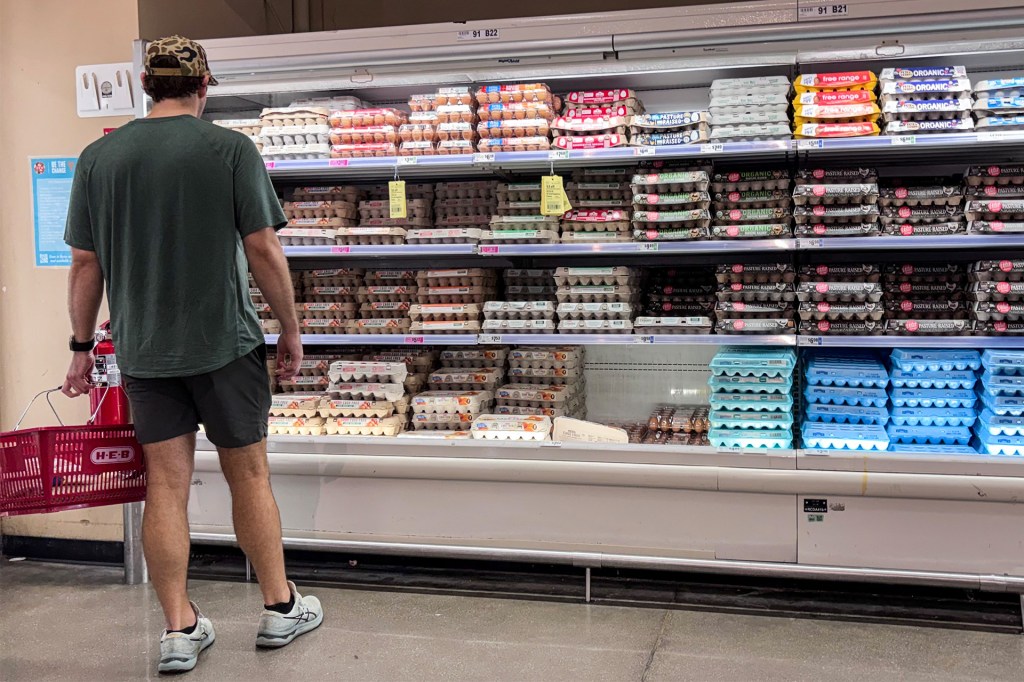 A shopper stands in front of a grocery store case filled with cartons of eggs.