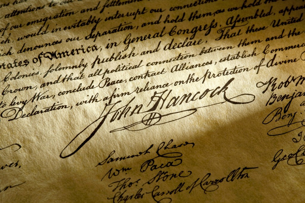 A close-up of the Declaration of Independence shows John Hancock’s large signature and other handwritten names.