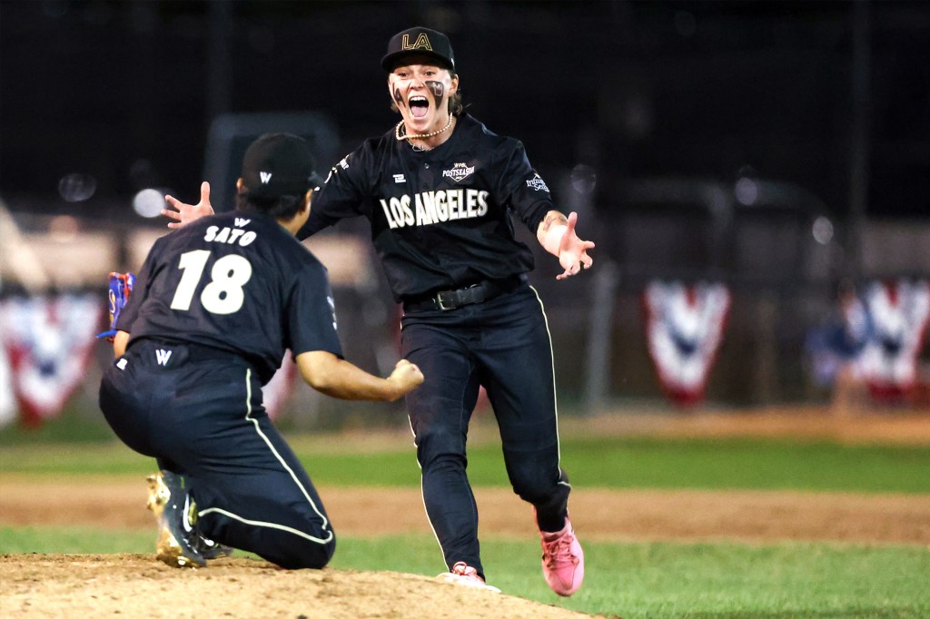 Two baseball players in black uniforms celebrate on the field, one running toward a kneeling teammate with her arms outstretched.