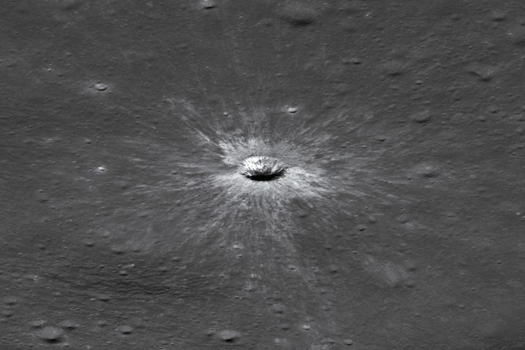 A crater surrounded by bright streaks marks the gray surface of the moon.
