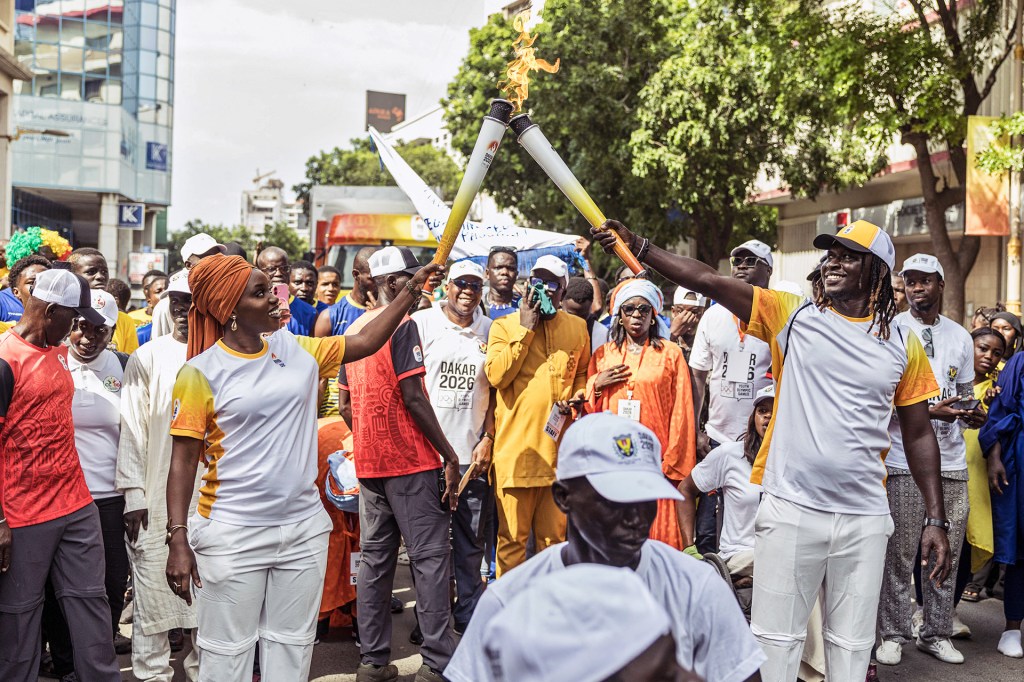 Two athletes hold flaming torches aloft as a crowd gathers around them.