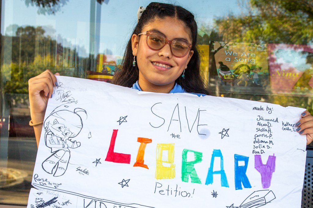 A girl holds a handmade poster calling for the library to be saved.