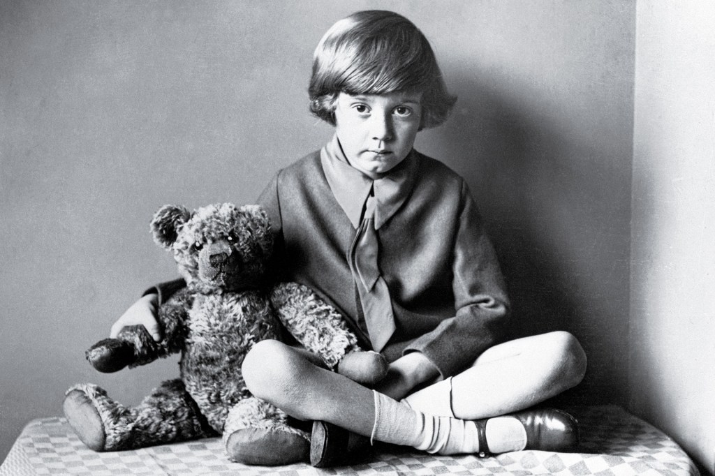 A black-and-white photograph shows a young boy sitting beside a teddy bear.