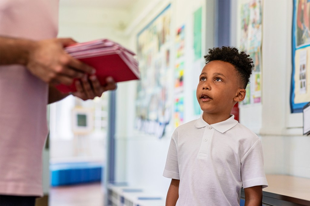 A boy looks up at an adult in a school hallway.