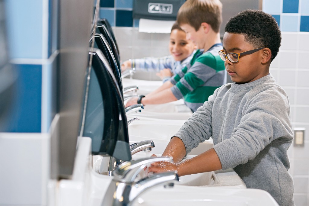 Children wash their hands at a row of sinks.