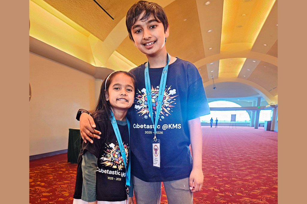 Two children wearing matching shirts and event lanyards pose together.