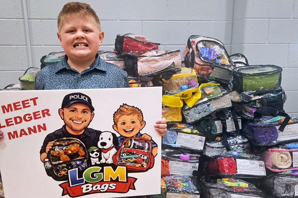 A boy holds a sign in front of a pile of clear backpacks.