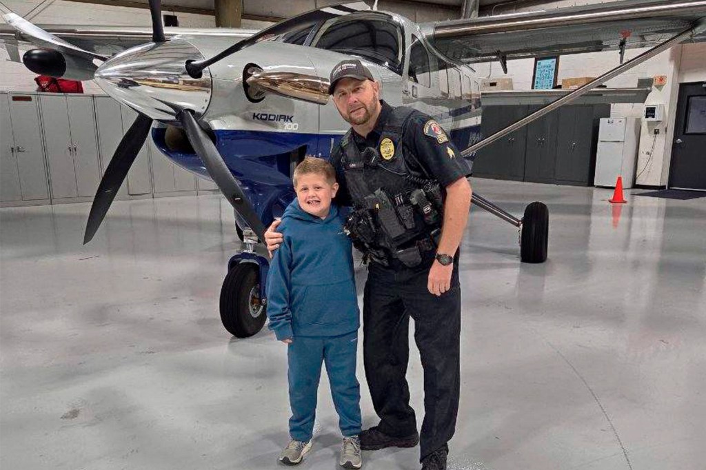 A boy poses with a police officer in front of a small airplane.