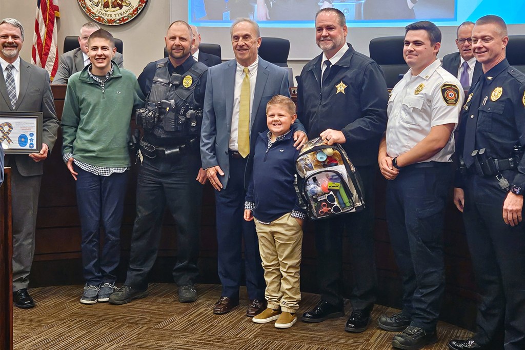 A boy stands with police, fire, and other officials at an awards ceremony.