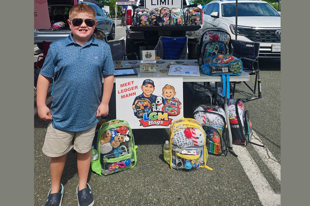 A boy wearing sunglasses stands beside a display of packed bags at an outdoor event
